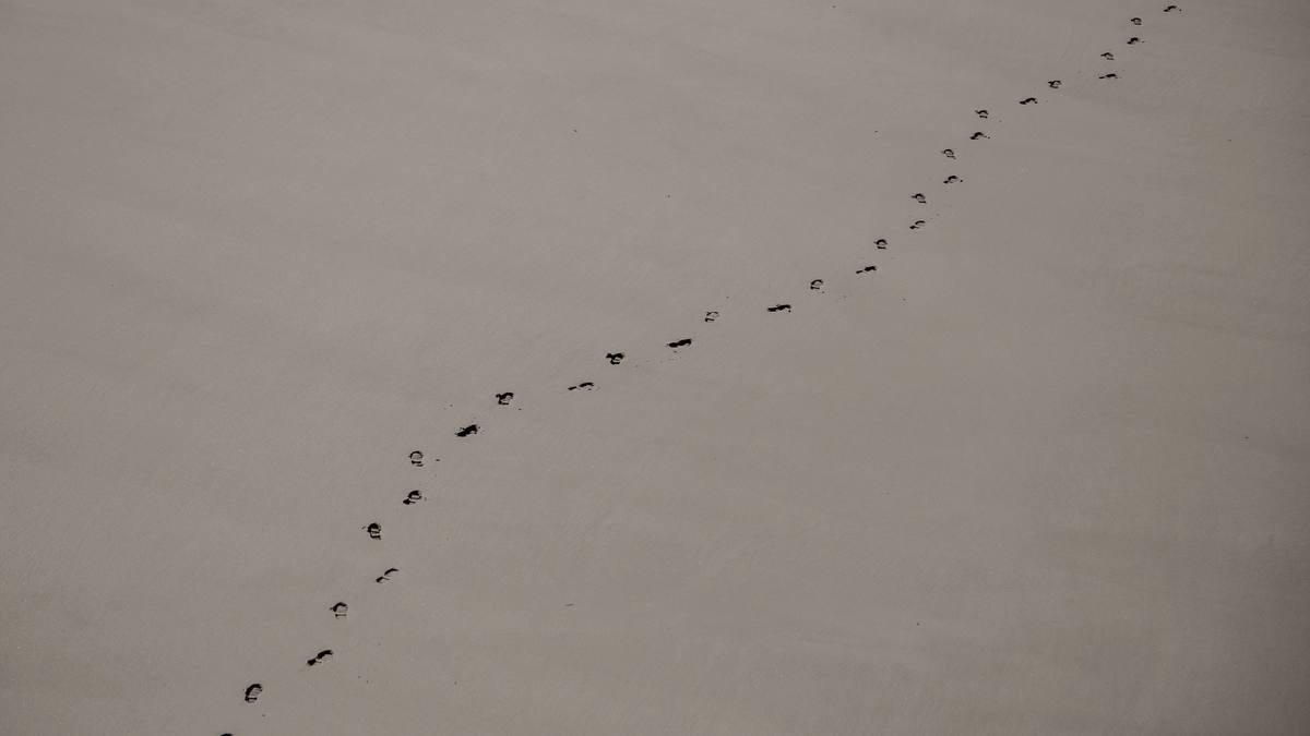 Een spoor voetstappen door zand dat doorloopt tot buiten beeld