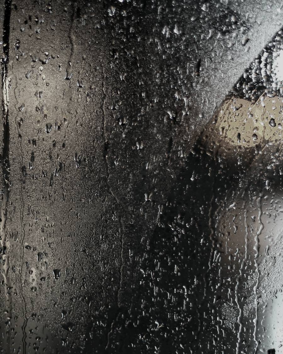 Regen op een ruit. Het licht erachter valt uiteen in de druppels